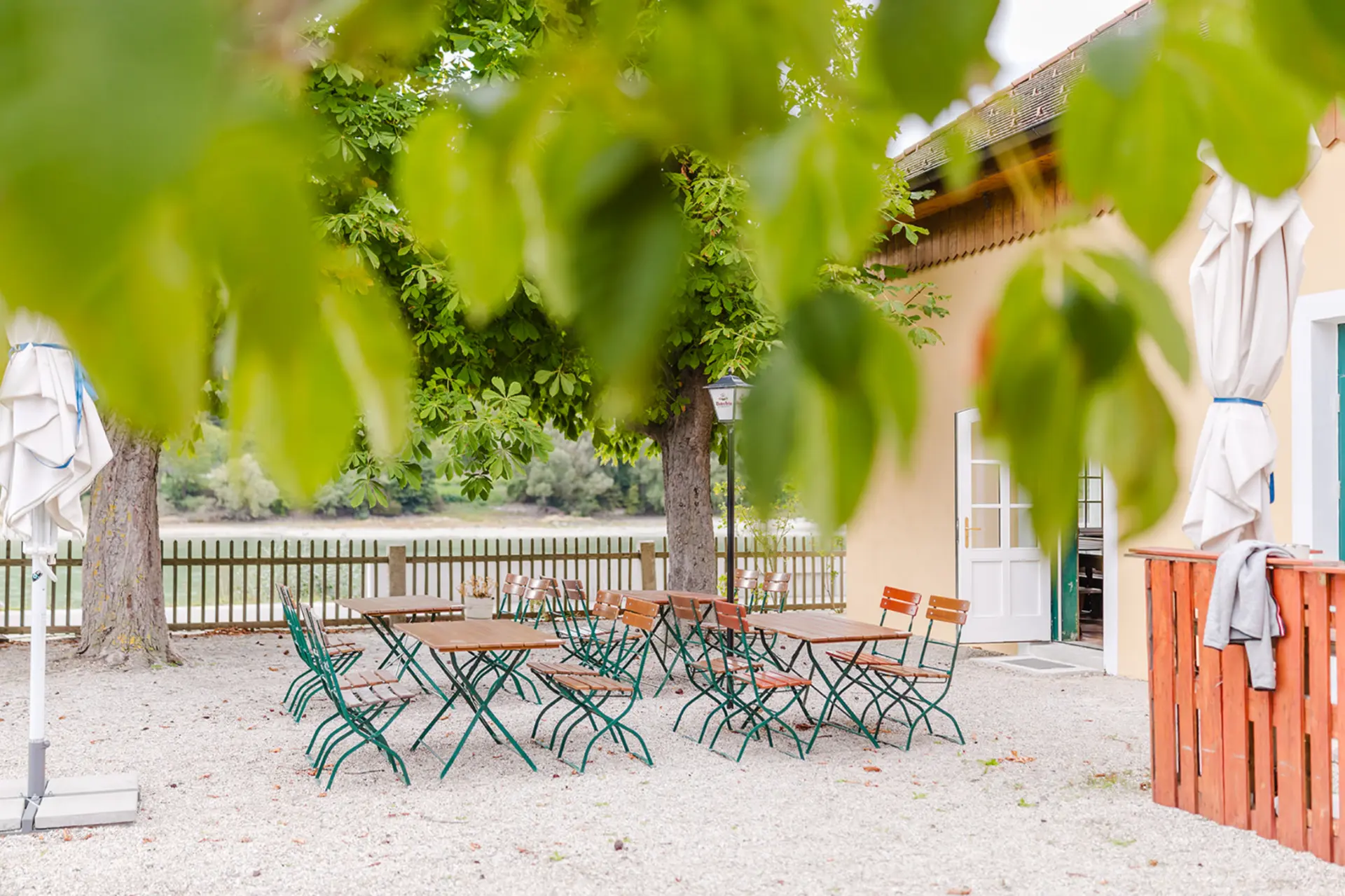 Gastgarten des Aggsteiner Hofs mit Tischen unter Kastanienbäumen und Blick zur Donau